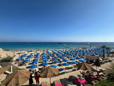 a beach with many blue umbrellas and the ocean at Ayia Napa GO SEA Sunny Apt with Terrace 5 min to Beach in Ayia Napa