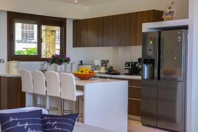 a kitchen with a stainless steel refrigerator and white chairs at Protaras El Greco Seafront Villa, Greco Mare in Protaras