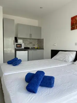a white bed with blue pillows on top of it at Midtown Napa Apartments in Ayia Napa