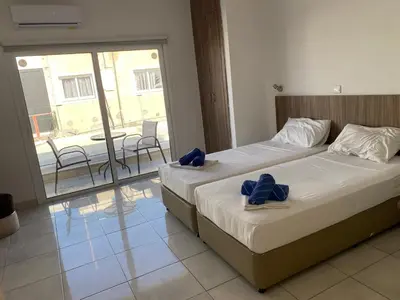 a bedroom with two beds and a balcony with a table at Midtown Napa Apartments in Ayia Napa