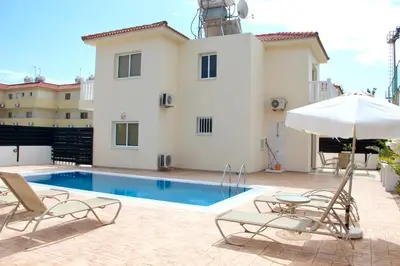 a swimming pool with two chairs and an umbrella at Villa Oceania in Ayia Napa