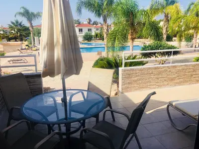 a table and chairs with a umbrella and a pool at Nissi 3 C4 Pool View Apt in Ayia Napa