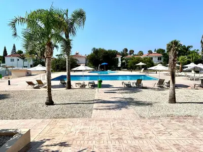 a swimming pool with palm trees and chairs and umbrellas at Nissi 3 C4 Pool View Apt in Ayia Napa