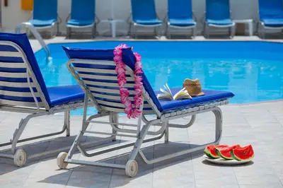 a swimming pool with a chair and a book and some watermelon at Paloma Hotel Apartments in Ayia Napa