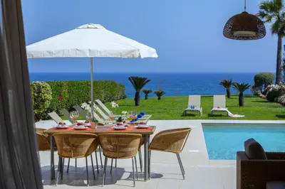a table with chairs and an umbrella next to a pool at Protaras Beachfront Villa Pietra in Protaras