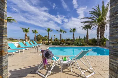 a pool with chairs and a table next to a swimming pool at Faros BeachFront Villa in Pervolia