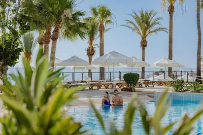 a man and woman standing in a swimming pool with palm trees at Golden Coast Beach Hotel in Protaras