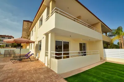 a white house with a patio and a lawn at Nissi Martha Apartment in Ayia Napa