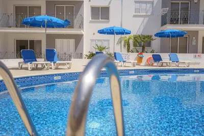 a swimming pool with blue chairs and umbrellas at Emily apartment in Paralimni