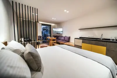 a bedroom with a white bed and a living room at Alinea Suites Limassol Center in Limassol