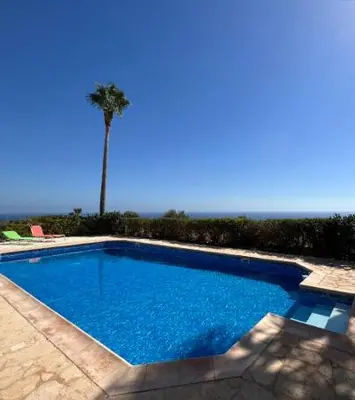a blue swimming pool with a palm tree in the background at Sunset Cliff Villa Panoramic Sea Views Private Heated Pool Included in Pissouri