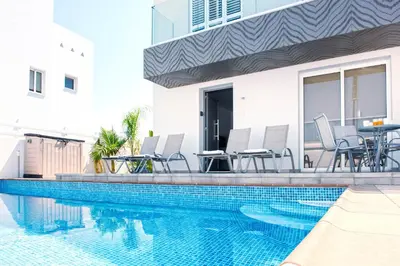 a swimming pool with chairs and a table next to a building at Nissini Nero, 3 bedroom villa with private pool, 5 min to the beach in Ayia Napa