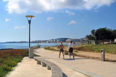 two people walking on a sidewalk next to the water at Villa Martha in Protaras