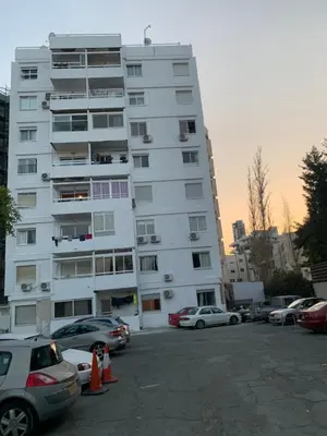 a tall white building with cars parked in a parking lot at Galaxy court modern apartment in Limassol