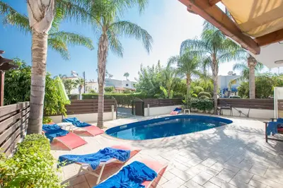 a swimming pool with chairs and palm trees at Villa Papantonia in Protaras