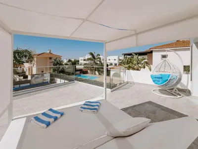 a white living room with a white couch and a balcony at Sunset Villa private complex heated pool in Ayia Napa