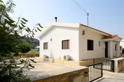 a white house with a black fence in front of it at Pissouri Bay Bungalow in Pissouri