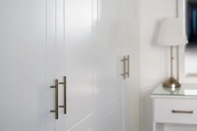 a white cabinet with metal handles next to a lamp at Krasas Beach Apts in Larnaka