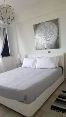a white bedroom with a bed with a picture of a tree at Krasas Beach Apartments in Larnaka