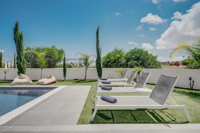a row of lounge chairs next to a swimming pool at Protaras Olivia Pearl Villa in Paralimni