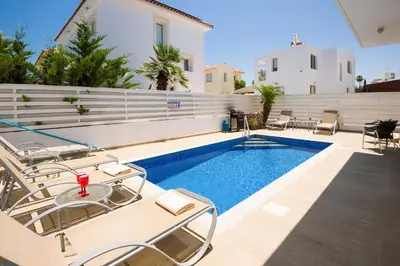 a pool with chairs and a table next to a house at Villa Blue Sky in Protaras