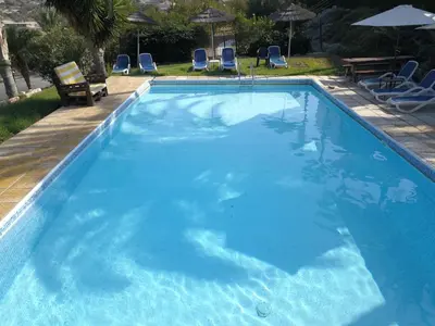 a large blue swimming pool with chairs and umbrellas at George Houses in Pendakomo