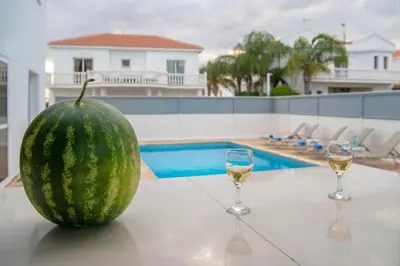 a melon sitting on a table with two glasses of wine at Villa Ruby Nissi Beach in Ayia Napa