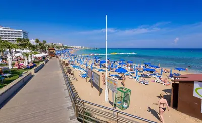 a beach with blue chairs and people on the beach at Protaras Centro Villa in Protaras