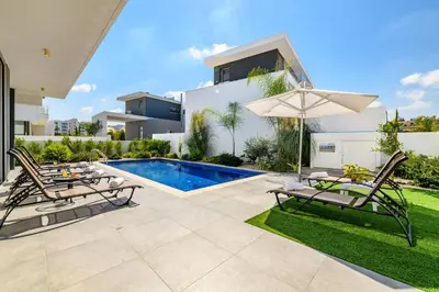 a backyard with a pool and two chairs and an umbrella at Olivine Waves in Protaras