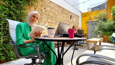 a woman sitting at a table reading a book at Le Mat Hostel in Larnaka
