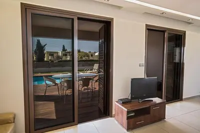 a living room with a sliding glass door with a television at Villa Petreris Dyo - Lovely 3 Bedroom Central Ayia Napa Villa With Pool in Ayia Napa