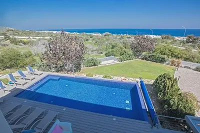 a swimming pool with chairs and the ocean in the background at Villa Kono Sunshine - Luxury 4 Bedroom Cape Greco - Villa Close To Beach in Protaras