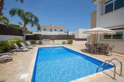 a swimming pool with chairs and a table and an umbrella at Villa Dafnis Chrysos - Modern 3 Bedroom Protaras Villa With Pool in Protaras