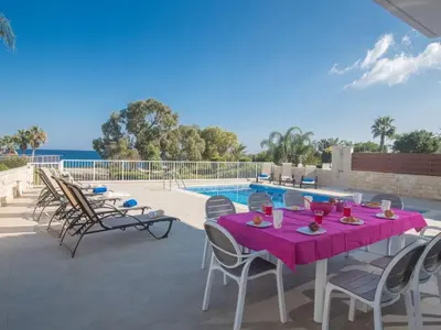 a table and chairs on a patio next to a pool at Villa Mesogi Seafront, Stunning 4Bdr Fontline Protaras in Protaras