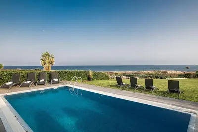 a swimming pool with chairs and the ocean in the background at Villa Fig Tree Bay Frontline,Luxury 4Bdr Sea-Front Protaras Villa With Pool in Protaras