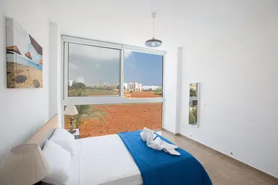 a bedroom with a bed with a blue blanket and a window at Villa Manta Platina - Brand New Luxury 3 Bedroom Protaras Villa in Protaras