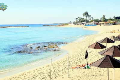a beach with umbrellas and people laying on the sand at Nissi Golden Sands Family Apartment in Ayia Napa
