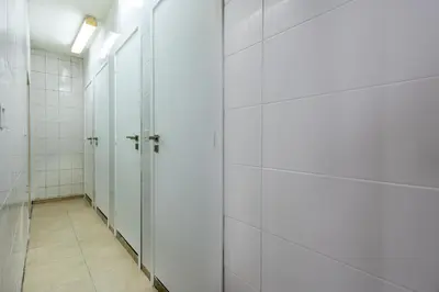 a corridor of stalls in a bathroom with white tiles at Bee Hostel in Limassol