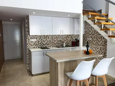 a kitchen with white cabinets and a counter with white chairs at Cozy Loft Apartment 2 in Ayia Napa