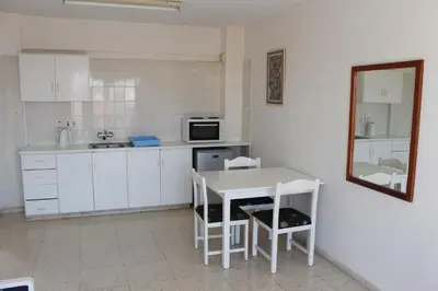 a kitchen with white cabinets and a table and chairs at Florea Hotel Apartments in Ayia Napa