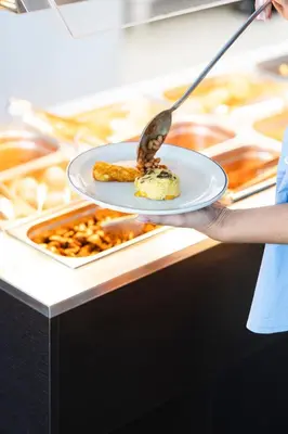 a person holding a plate with food on a counter at TSANotel in Limassol
