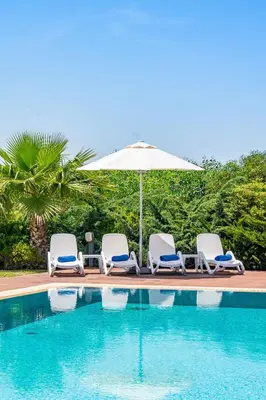 a group of chairs and an umbrella next to a swimming pool at Seafront Villa Cecelia by Ruidoso Luxury in Ayia Napa