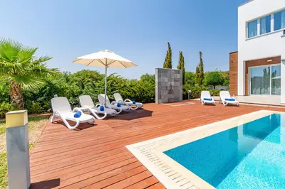 a pool with chairs and an umbrella next to a house at Villa Dione by Ruidoso Luxury in Ayia Napa