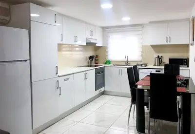 a white kitchen with white cabinets and a table at Seafront - 2 bedroom Modern in Limassol