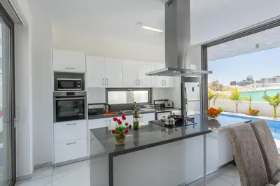 a kitchen with white cabinets and a large window at Protaras Royal Pearl Villa 7 in Protaras