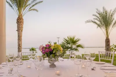 a table with glasses and flowers and palm trees at Radisson Beach Resort Larnaca in Larnaka