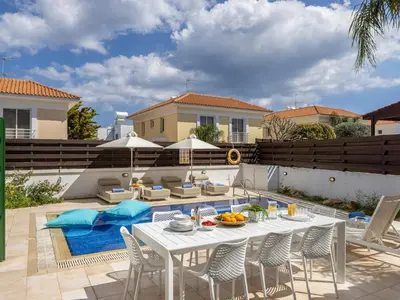 a patio with a white table and chairs and a pool at Villa Eftihia in Protaras