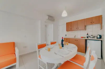 a kitchen with a white table and orange chairs at Christos Napa Self Serviced Apartments in Ayia Napa