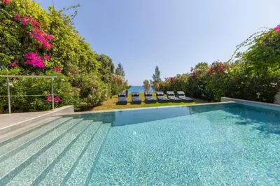 a swimming pool with chairs and flowers and the water at Villa Adalia in Protaras