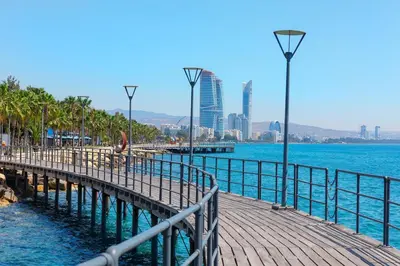 a wooden pier next to the water with a city at 1 bedroom flat, prime location near sea, sleeps 4 in Limassol